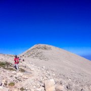 Randonneurs en plein effort sur un sentier rocheux menant au sommet d’une montagne en Crète, sous un ciel bleu intense et dégagé.