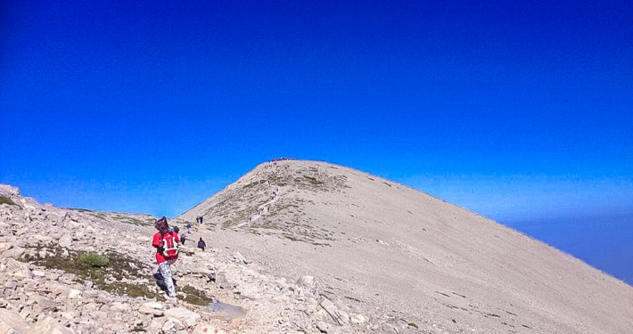 Randonneurs en plein effort sur un sentier rocheux menant au sommet d’une montagne en Crète, sous un ciel bleu intense et dégagé.