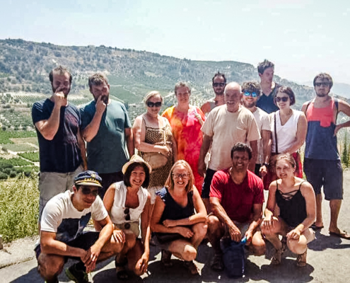 Groupe de voyageurs posant devant un paysage vallonné typique de la Crète, avec des vignobles et des oliveraies s’étendant à l’horizon sous un ciel ensoleillé.