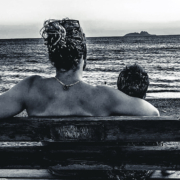 Vue arrière d’une femme et d’un enfant assis sur un banc face à la mer, contemplant l’horizon et une petite île au loin, capturant un moment paisible au bord de l’eau en Crète.