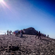 Groupe de randonneurs au sommet d’une montagne en Crète, sous un ciel bleu clair avec une vue panoramique sur les environs rocheux et ensoleillés.