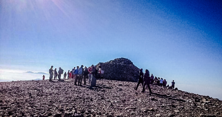 Groupe de randonneurs au sommet d’une montagne en Crète, sous un ciel bleu clair avec une vue panoramique sur les environs rocheux et ensoleillés.