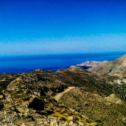 Vue panoramique des montagnes rocheuses de Crète avec en arrière-plan la mer Égée sous un ciel bleu éclatant, représentant la beauté naturelle de l’île.