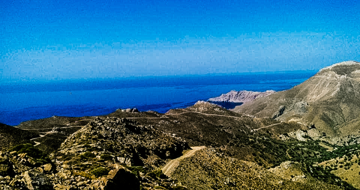 Vue panoramique des montagnes rocheuses de Crète avec en arrière-plan la mer Égée sous un ciel bleu éclatant, représentant la beauté naturelle de l’île.